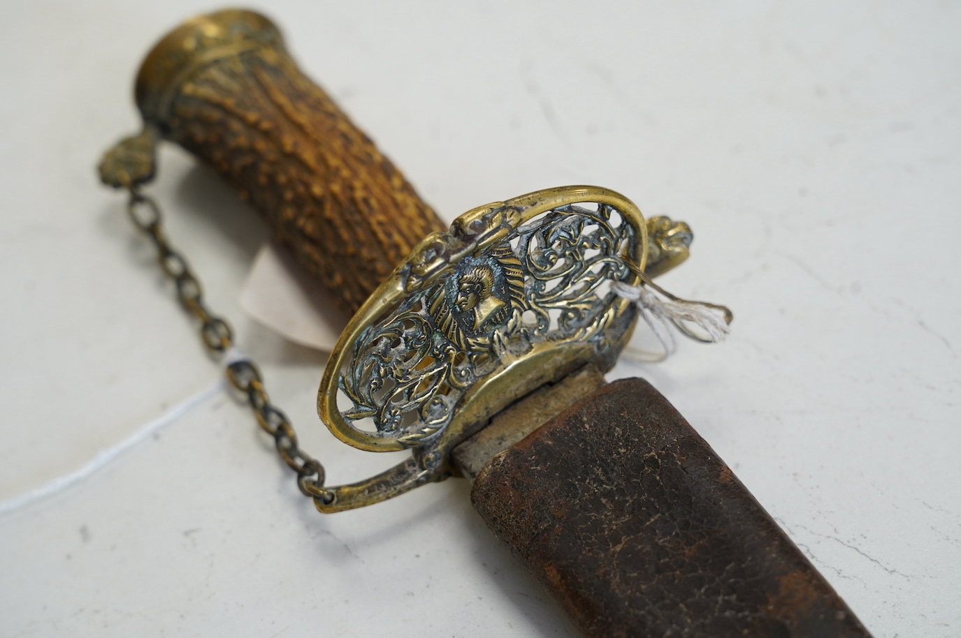 A William III English hunting hanger with pierced brass mounts, stag horn grip, blade struck with king’s head, in its leather scabbard, blade 45cm. Condition - worn, knuckle bow replaced with chain and chape missing to s